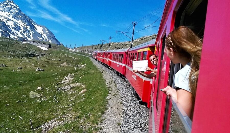A passenger leaning from the window of a red alpine train